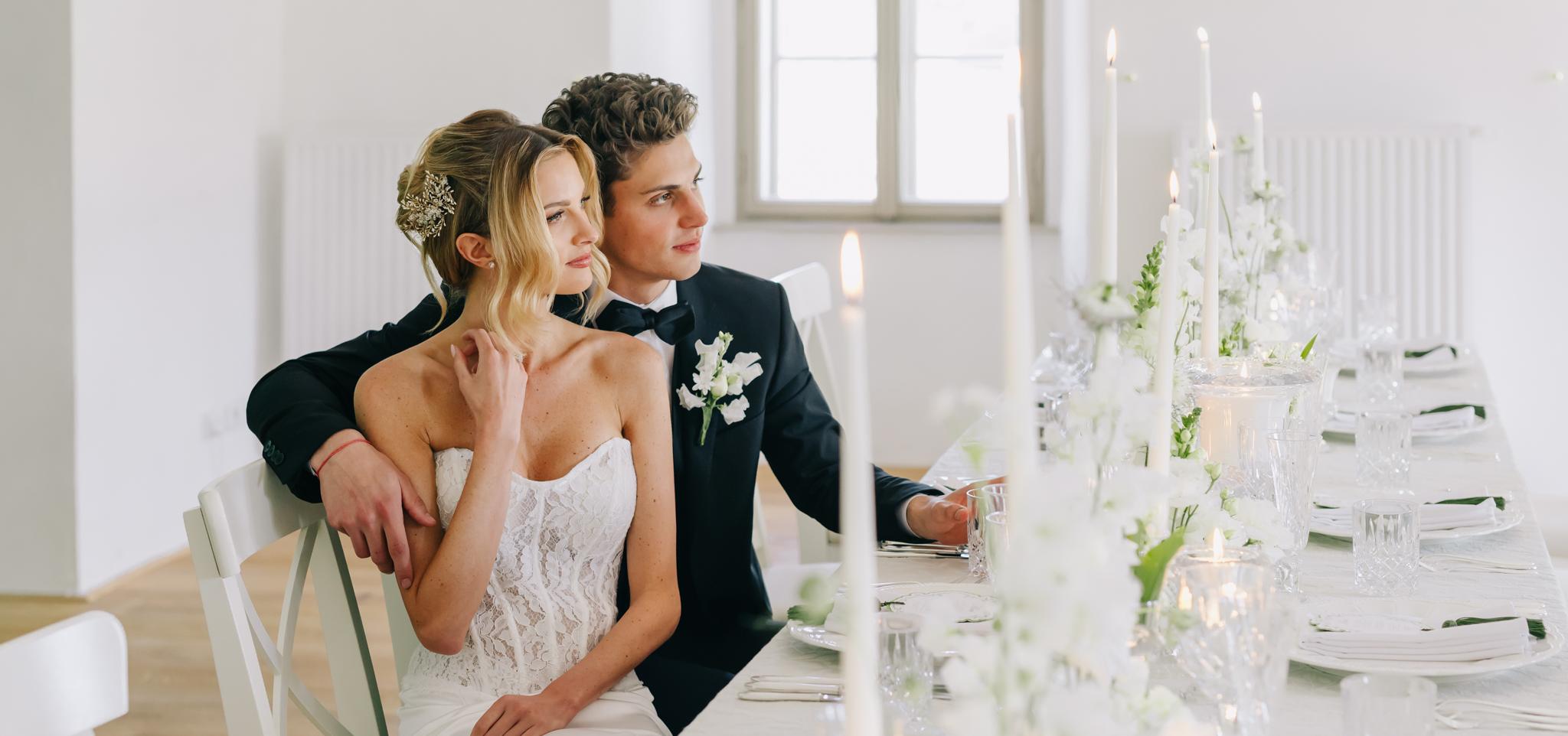 Nevesta so závojom a perlovými náušnicami stojí tvárou pri ženíchovi, obaja sú zachytení v jemnom romantickom momente v exteriéri.