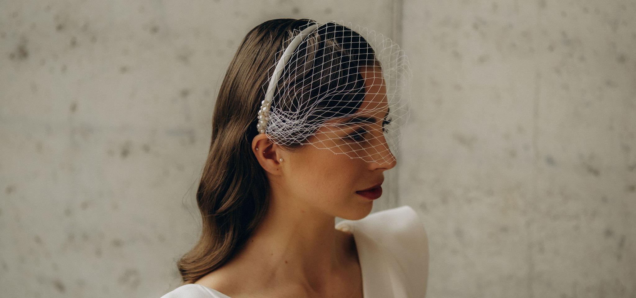 Nevesta s kvetinovými náušnicami stojí pri ženíchovi, ich pohľady smerujú mimo objektív, zachytení v exteriéri medzi stromami.