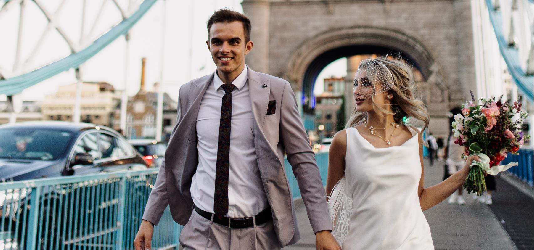 Nevesta počas príprav sedí na posteli v bielom župane, smeje sa a drží pohár so šampanským, vo vlasoch má výraznú aplikáciu s lístkami a perlami.