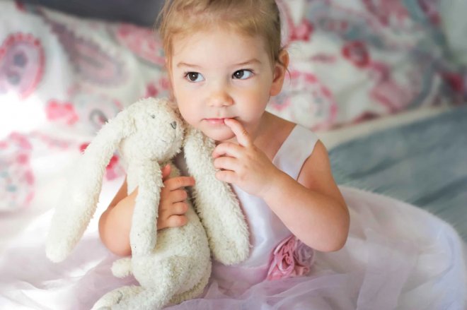 dievčatko v ružových šatách s bielym zajačikom moji na posteli
