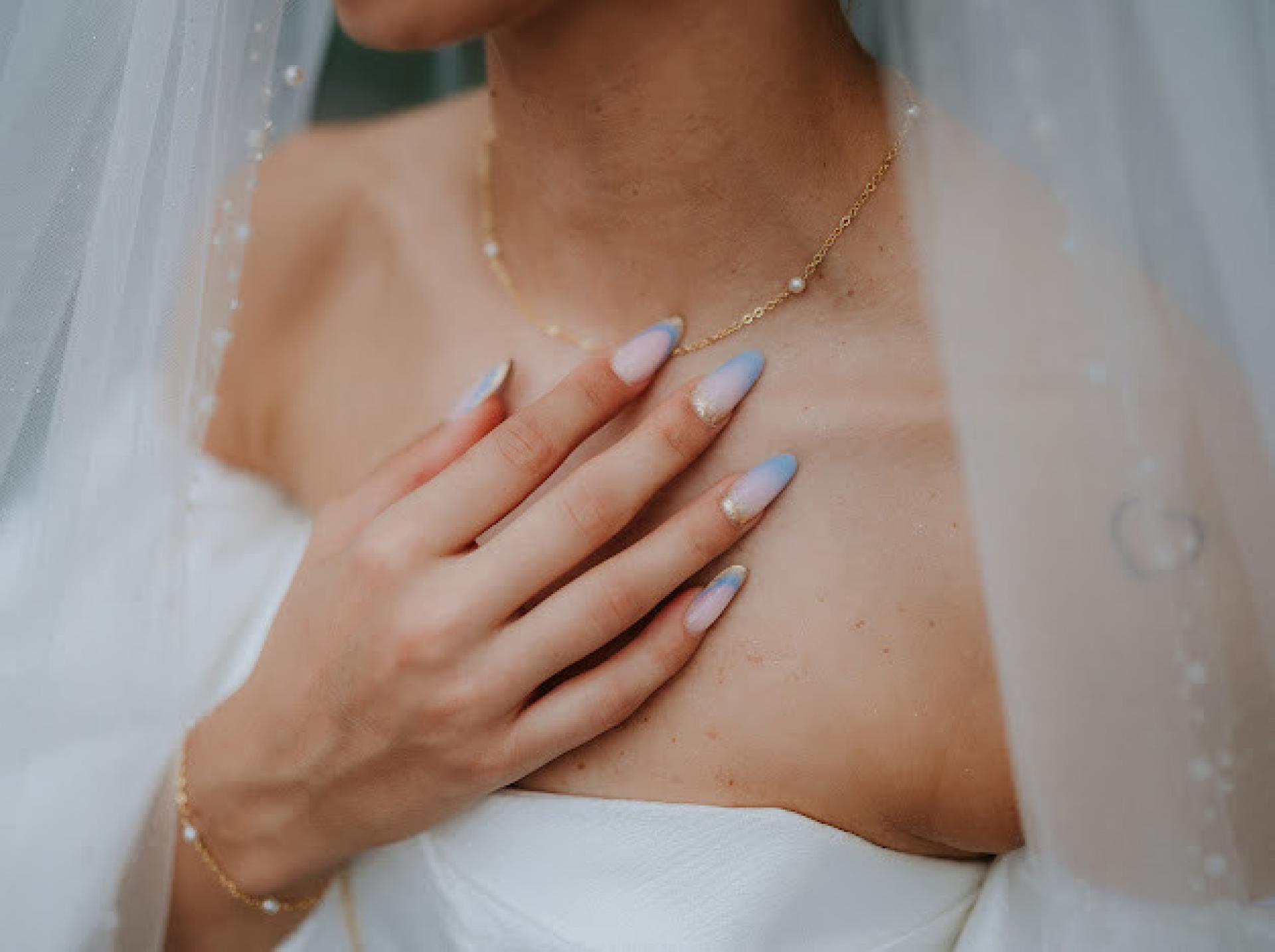 detail svadobnej retiazky na krku nevesty s peknou francúzskou manikúrou s modrými detailami