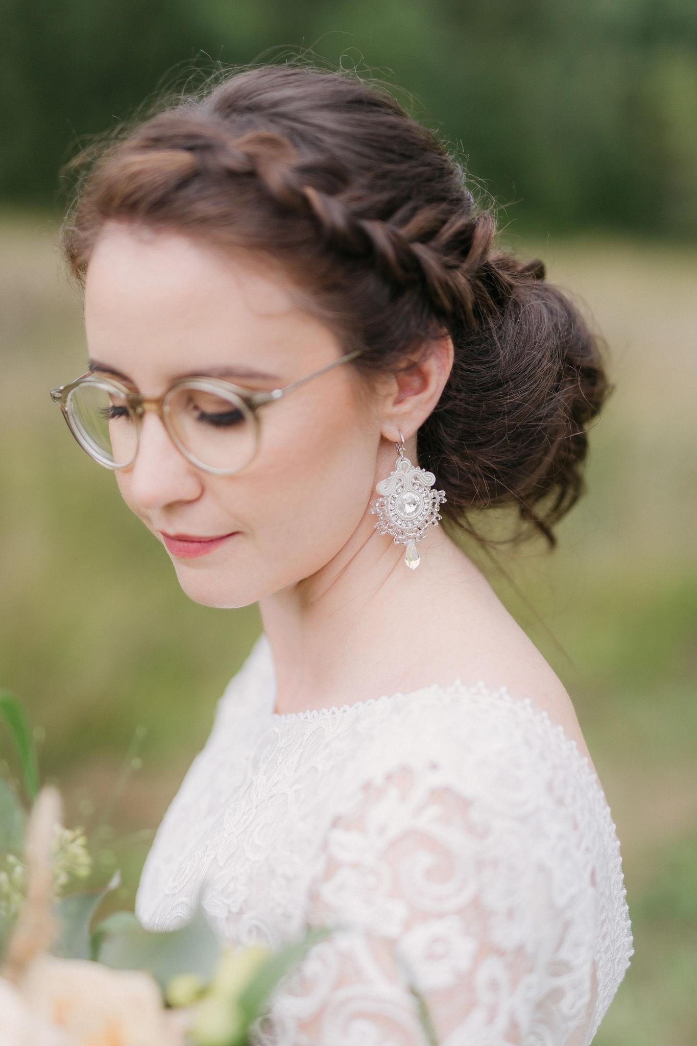 Nevesta v čipkovaných svadobných šatách s okuliarmi, detailný portrét z profilu so zdobenými svadobnými náušnicami.